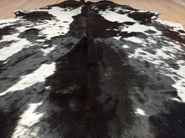 Czarno-brązowo-biała skóra bydlęca w cętki rozłożona na jasnej podłodze - zbliżenie na lśniącą sierść