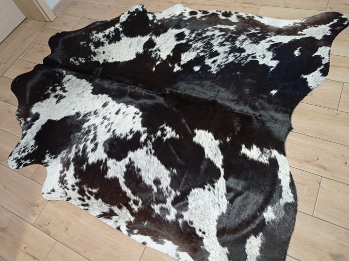 Czarno-brązowo-biała skóra bydlęca w cętki rozłożona na jasnej podłodze - dekoracyjneskory.pl