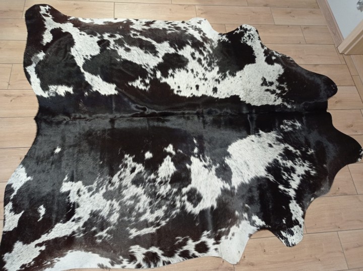 Czarno-brązowo-biała skóra bydlęca w cętki rozłożona na jasnej podłodze - dekoracyjneskory.pl