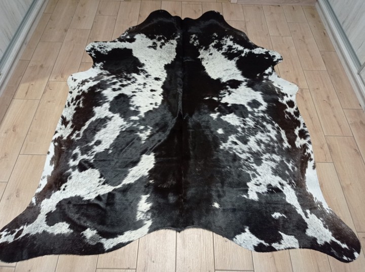 Czarno-brązowo-biała skóra bydlęca w cętki rozłożona na jasnej podłodze - dekoracyjneskory.pl
