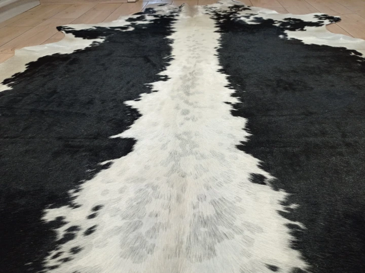 Naturalna skóra bydlęca CZARNO-KREMOWA 210x175 cm rozłożona w dużym salonie  - zbliżenie na lśniący włos -  dekoracyjneskory.pl